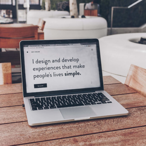 A laptop sitting on a wooden table with the screen saying, 'I design and develop experiences that make people's lives simple.'