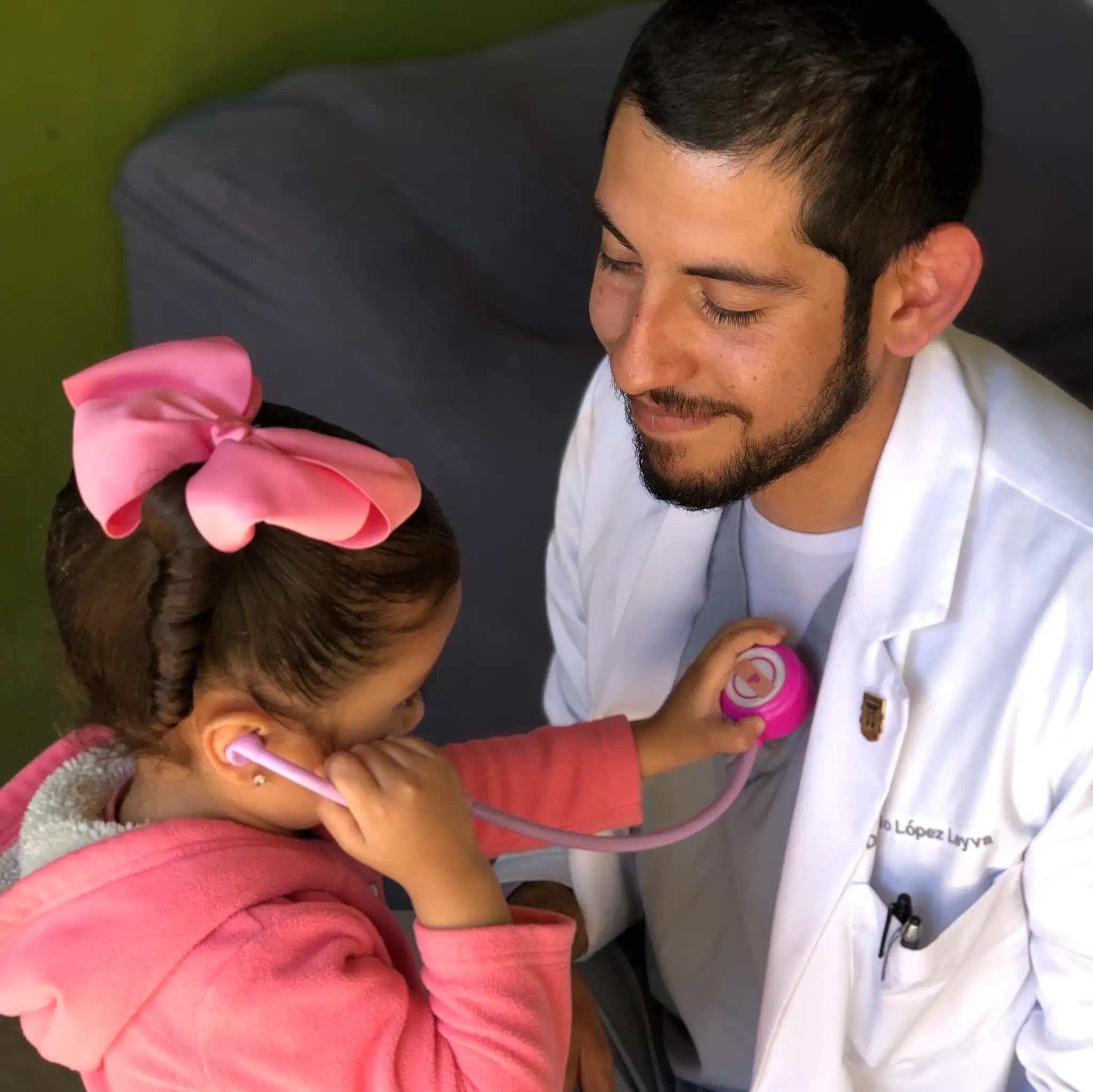 Pediatrician letting a girl test him with stethoscope toy