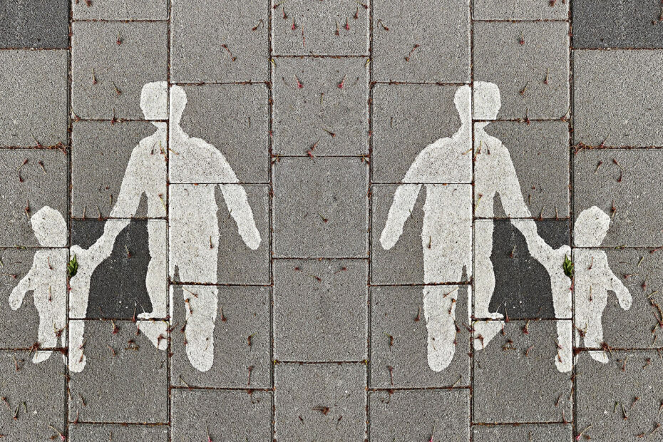On a grey sidewalk, a silhouette of a child and parent holding hands are painted in white
