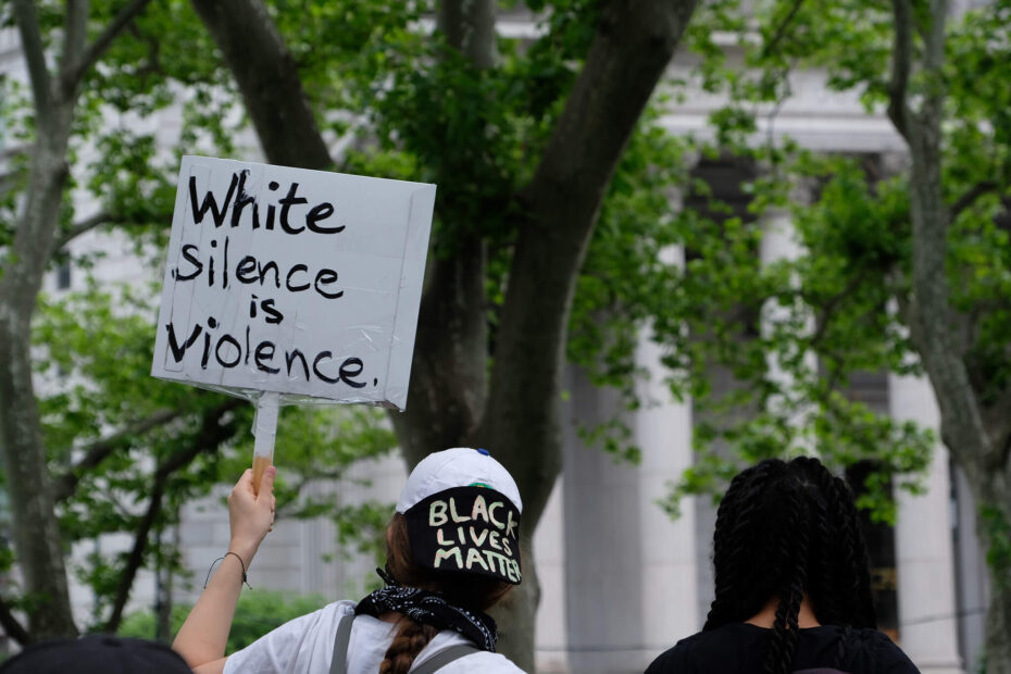 Woman with "Black Lives Matter" hat holding a banner with "White Silence is Violence"